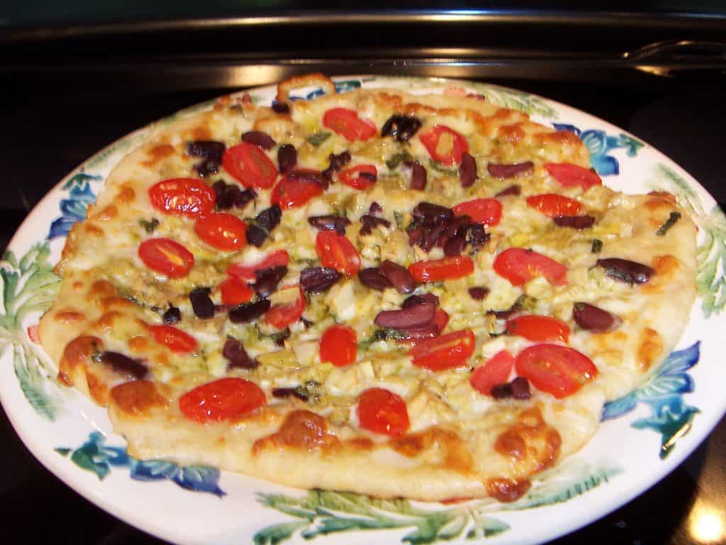 Golden pizza with tomatoes, pesto, black olive on a round platter