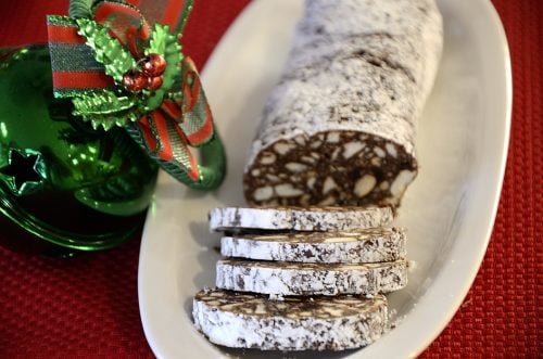 Chocolate log cut into slices with Christmas ornaments around the serving dish.