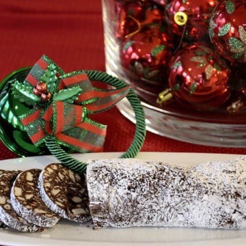 Chocolate log cut into slices with Christmas ornaments around the serving dish.
