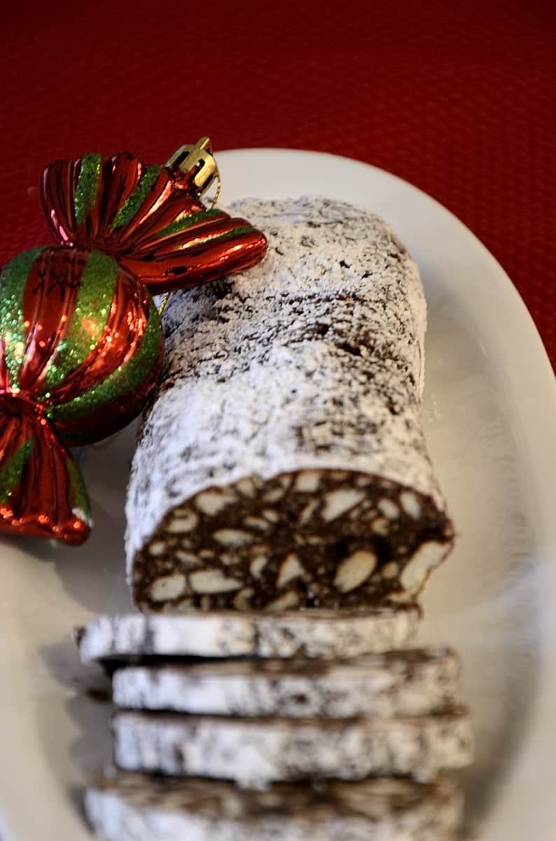 Chocolate log cut into slices with Christmas ornaments around the serving dish.