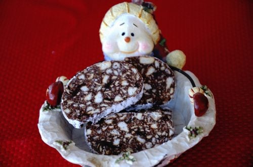 Chocolate log cut into slices in a Christmas serving dish.