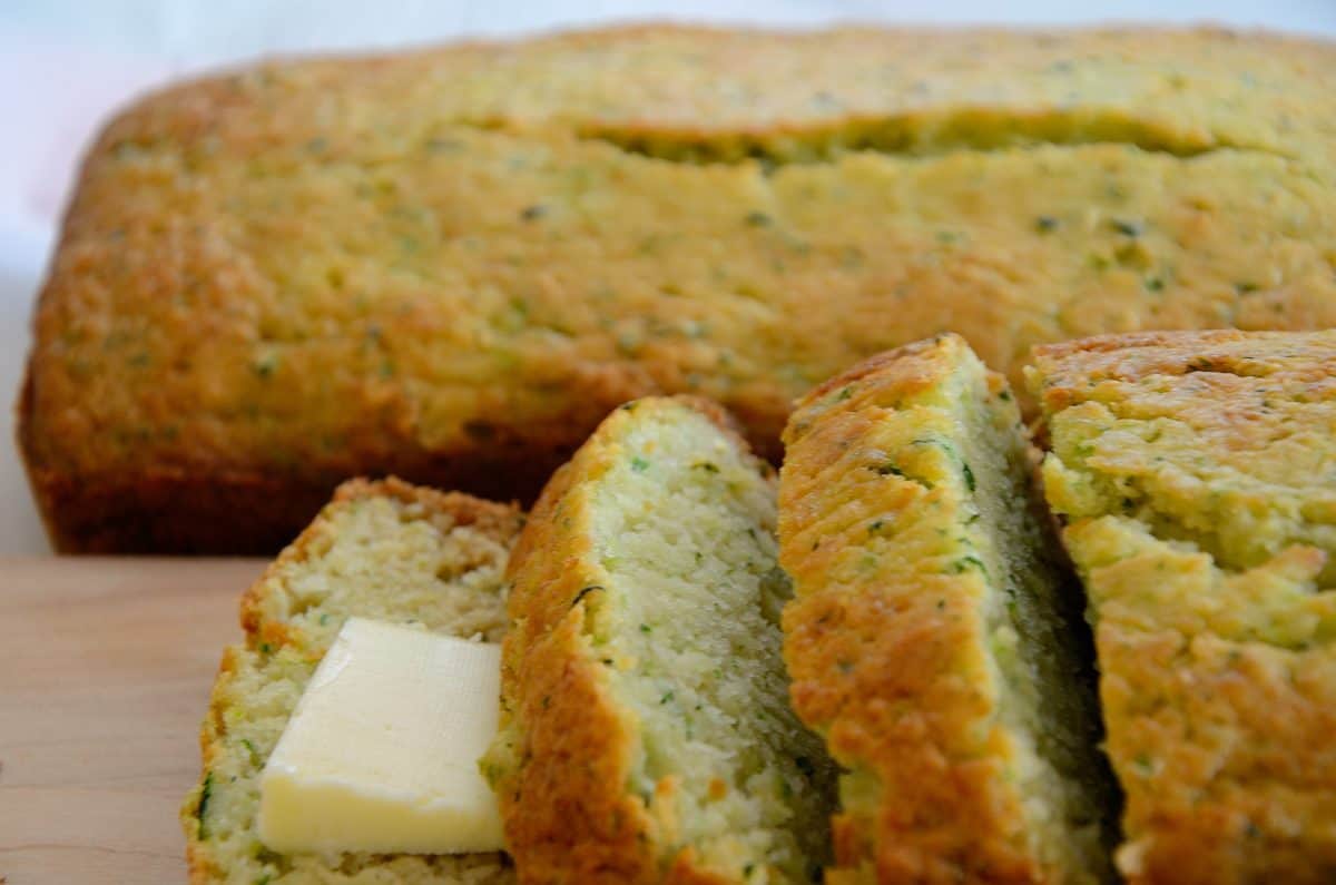 Two loaves of lemon yellow zucchini bread, some sliced with a pat of butter.