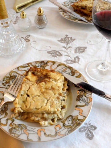 Square of Mushroom Marsala Lasagna on a Christmas plate with a glass of red off to the side.
