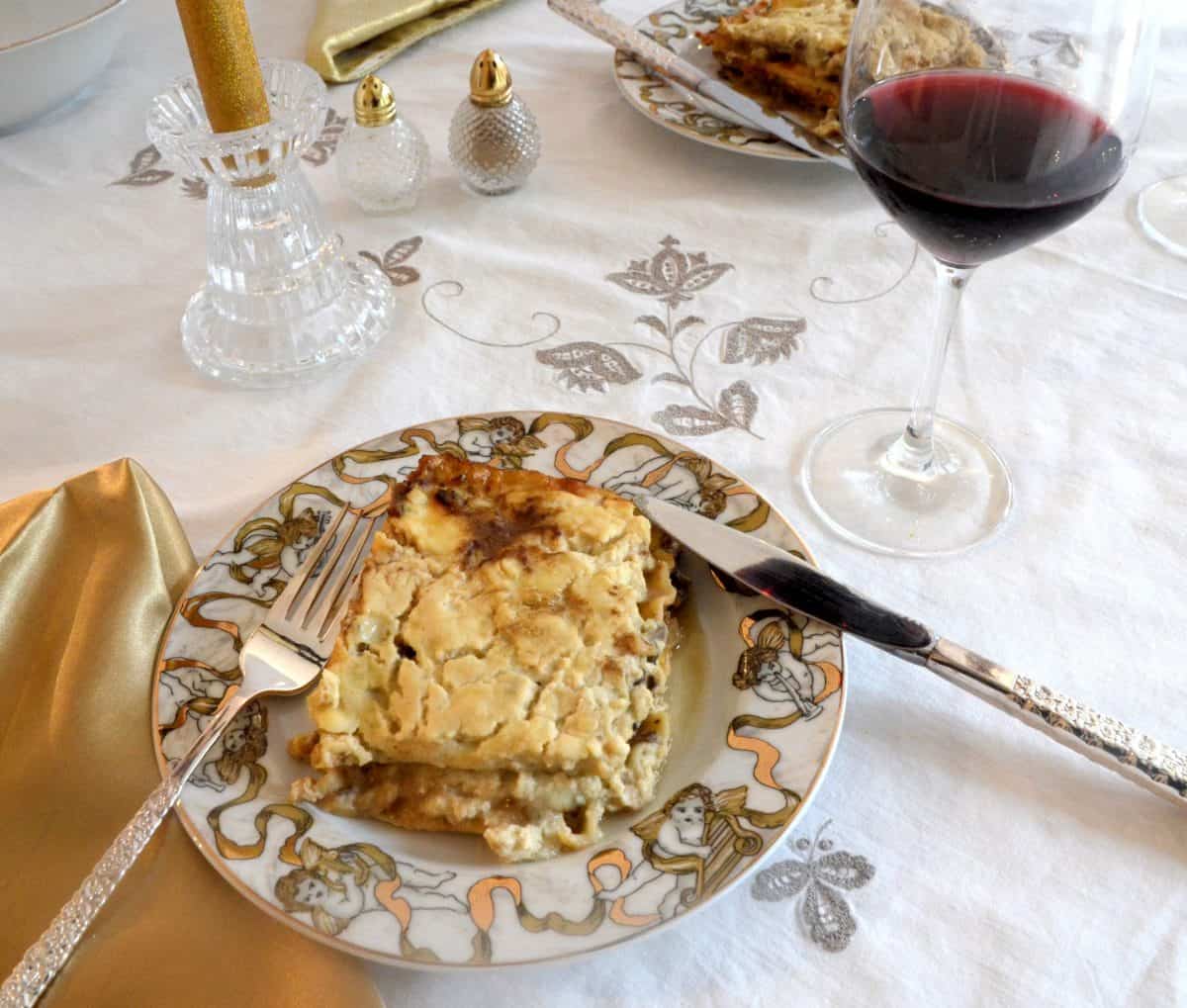 Square of Mushroom Marsala Lasagna on a Christmas plate with a glass of red off to the side.