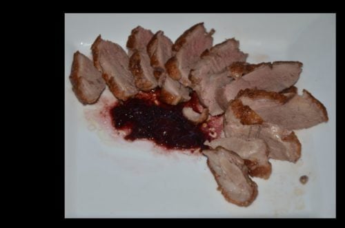 Sliced duck breast fanned out on a plate with cherry port sauce