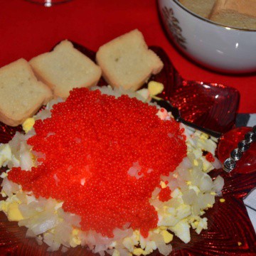 A plate with chopped hard boiled egg topped with sweet onion and red lumpfish caviar.