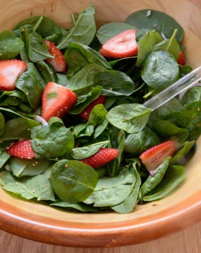 Spinach and strawberry slices in a wooden salad bowl.