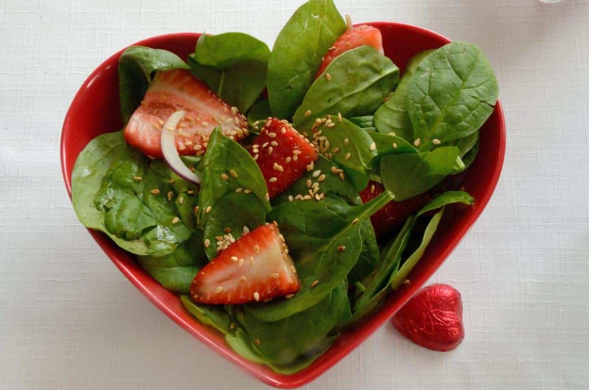 Spinach and strawberry slices in a red hear shaped salad bowl.