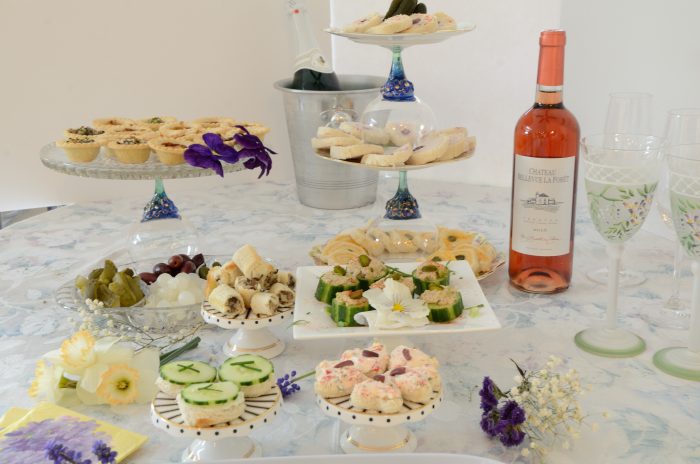 A buffet table laden with tea sandwiches, open face cucumber sandwiches, pastries and Rosé wine.