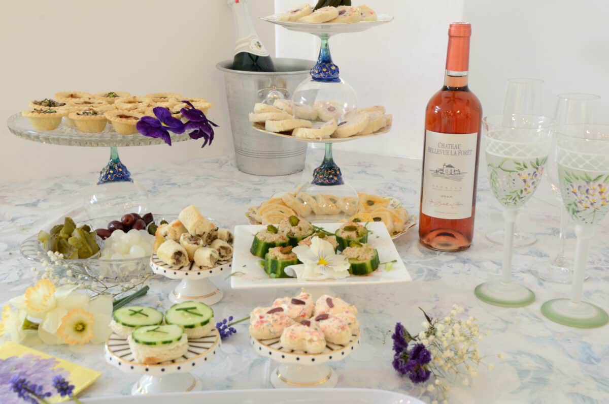 A buffet table laden with tea sandwiches, open face cucumber sandwiches, pastries and Rosé wine.