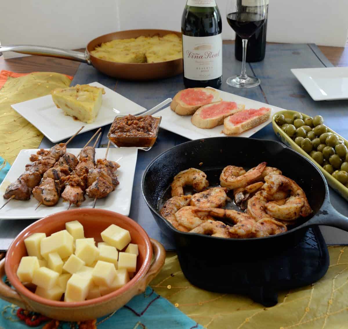 Table full of Spanish tapas and rioja wines, including pan con tomate, manchego cheese cubes, Spanish tortilla and marinated olives.