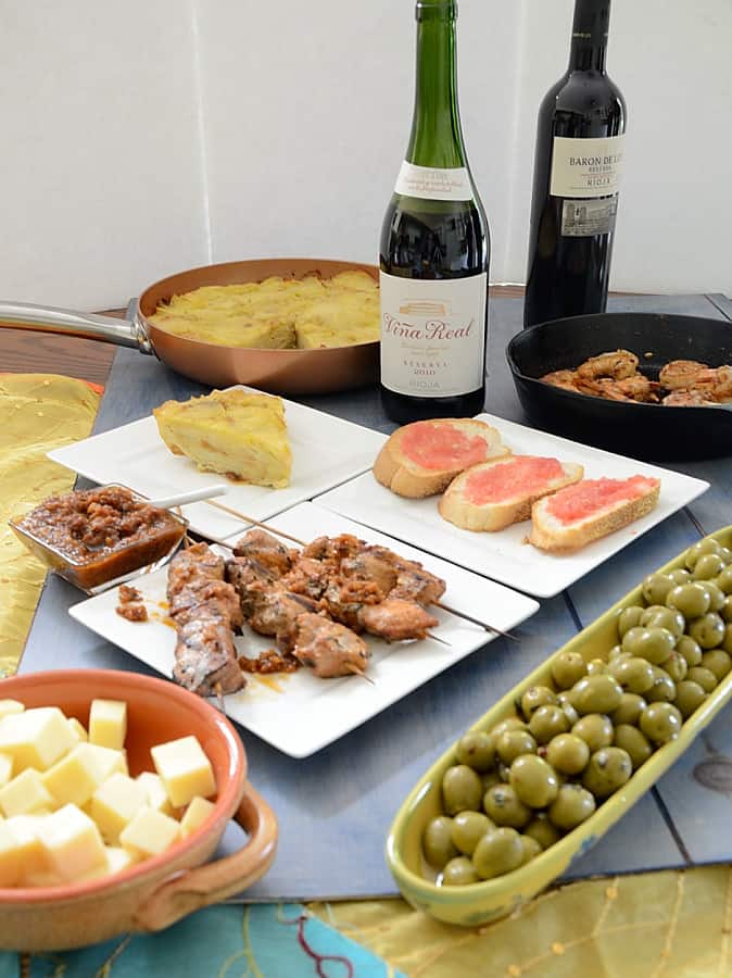 Table full of Spanish tapas and rioja wines, including pan con tomate, manchego cheese cubes, Spanish tortilla and marinated olives.
