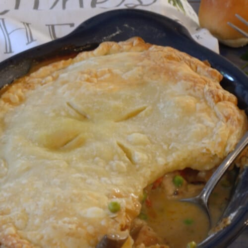 Baked chicken pot pie with spoon showing rich gravy, chicken and vegetables.