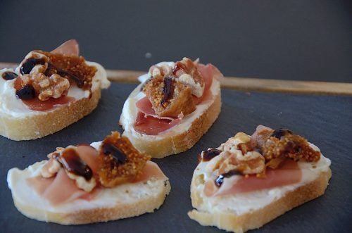 French baguette slices topped with cream cheese and a piece of prosciutto, dried fig and walnut