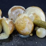 Baby potatoes with raclette cheese melted over them and garnished with gherkins and cocktail onions.