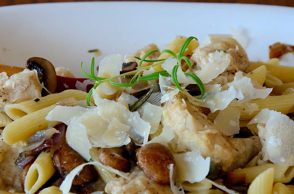 Penne in a bowl with chicken, rosemary and mushrooms.