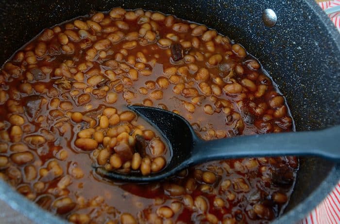 Deep browened baked beans in casserole with serving spoon