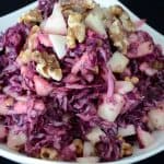 Red cabbage salad garnished with apple and walnuts in a bowl.