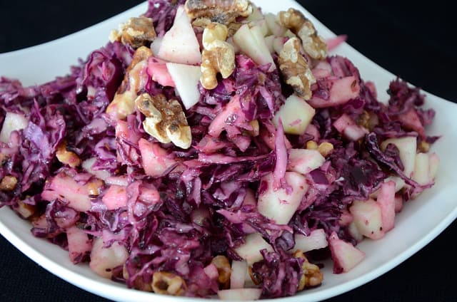 Red cabbage salad garnished with apple and walnuts in a bowl.