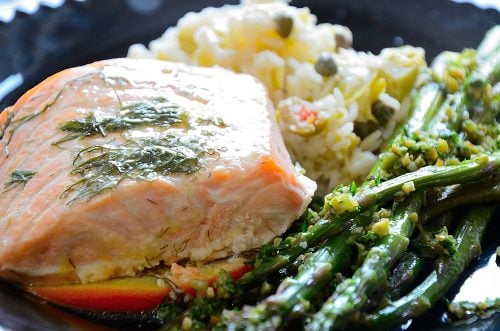 Salmon fillet on orange slices with fennel fronds plated with asparagus and rice