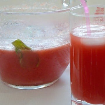 A glass with a straw and a pitcher containing strawberry Switchel drink.