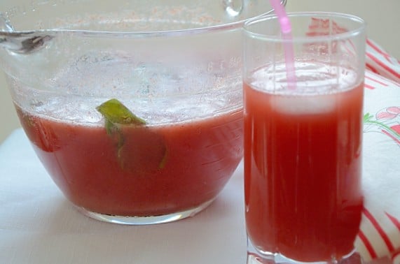 A glass with a straw and a pitcher containing strawberry Switchel drink.