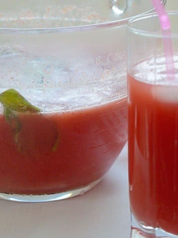 A glass with a straw and a pitcher containing strawberry Switchel drink.