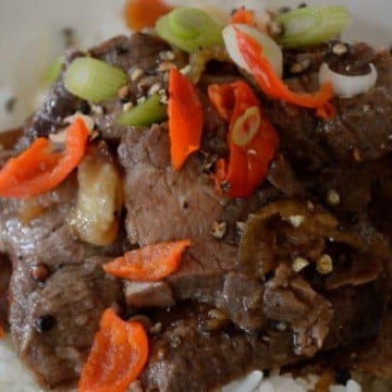 Close up of Flank steak strips with pepper and green onion garnish in black pepper sauce.