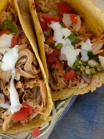 Two tacos filled with pulled pork and garnished with pico de gallo and lime crema