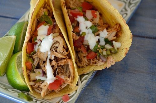 Two tacos filled with pulled pork and garnished with pico de gallo and lime crema
