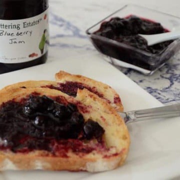 Toast with blueberry jam on a plate with jam jar behind.