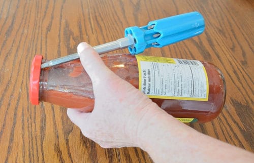A picture of a glass bottle with a lid and a screwdriver tip inserted under the lid