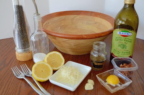 Table set with wooden salad bowl, lemon, anchovies, parmesan, egg yolk.