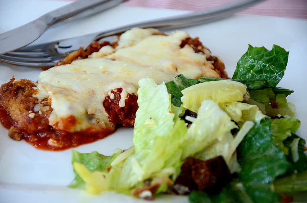 Eggplant Parmigiana scallop beside caesar salad on a plate.