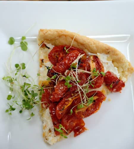 Piece of tart filled with roasted tomatoes and garnished with microgreens