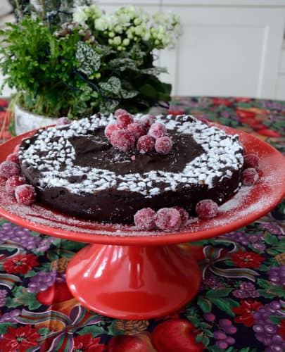 Round brownie cake on a pedestal, with sifted icing sugar and sugared cranberries for garnish