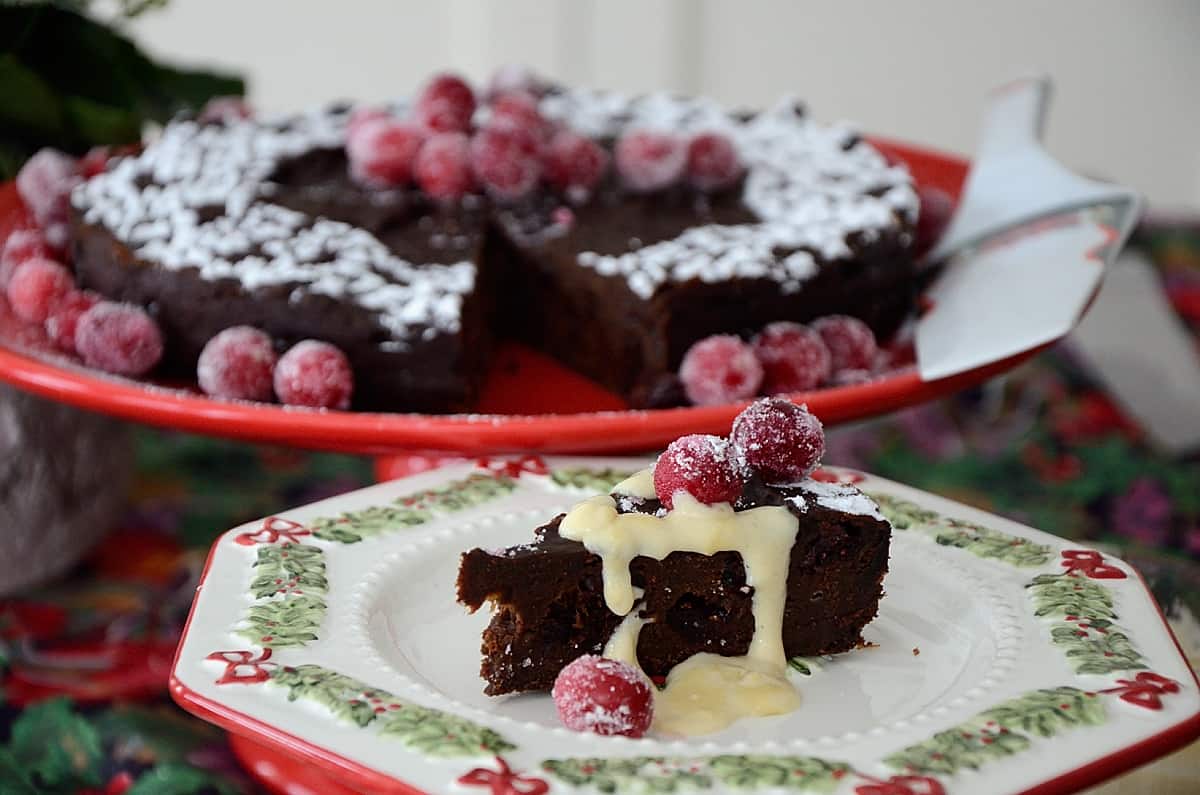 Round brownie cake on a pedestal, with sifted icing sugar and sugared cranberries for garnish
