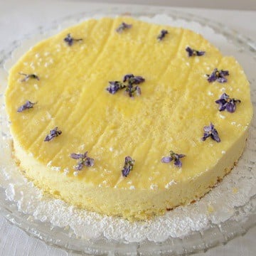 Ricotta cake on a bed of icing sugar decorated with candied violets