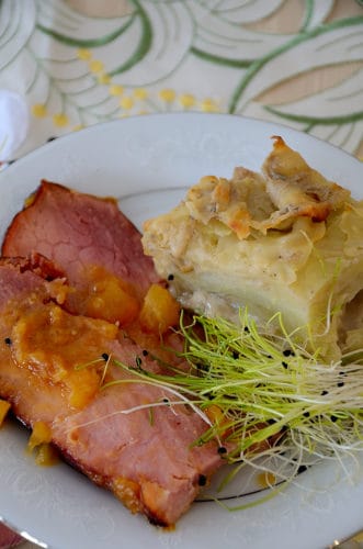 Plate with a serving of scalloped potatoes and a slice of ham with brown sugar pineapple glaze and garnished with microgreens. 