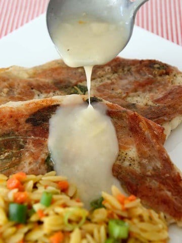 2 chicken cutlets with crispy sage and prosciutto on a plate with carrot orzo