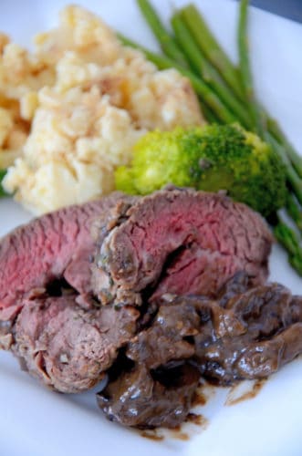 Plate with a slice of rare beef with mushroom sauce and mashed potatoes with caramelized shallots in the background