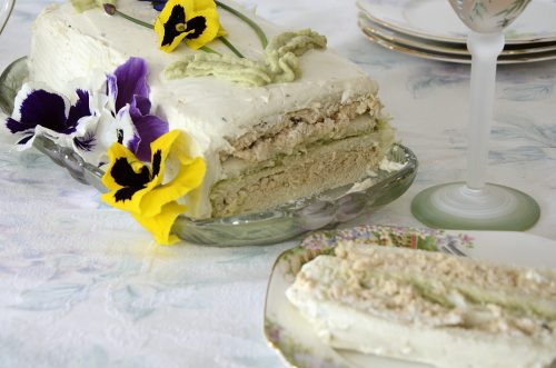 Sliced Chicken Avocado Sandwich cake decorated with purple and yellow pansies, chives for stems and piped avocado mousse for leaves