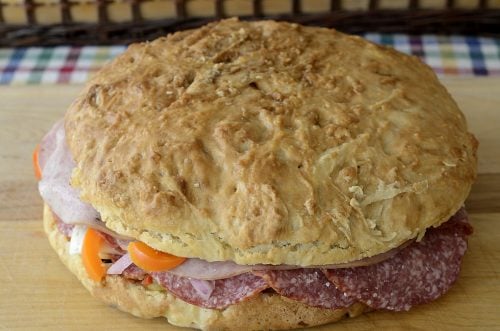 Round loaf of bread with many layers of cured meats and cheese and olive salad