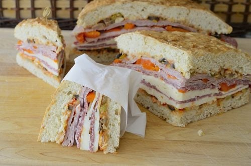 Wedges of muffuletta with cure meats, cheeses and peppers, wrapped in parchment paper