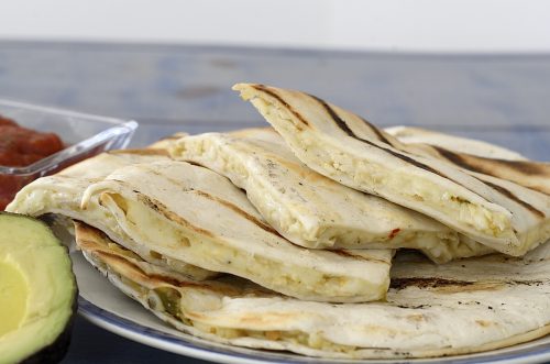 Quartered quesadillas on a plate with avocado on the side