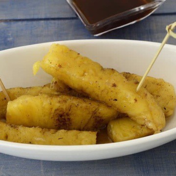 Grilled pineapple spears in a dish with spiced rum sauce drizzled over