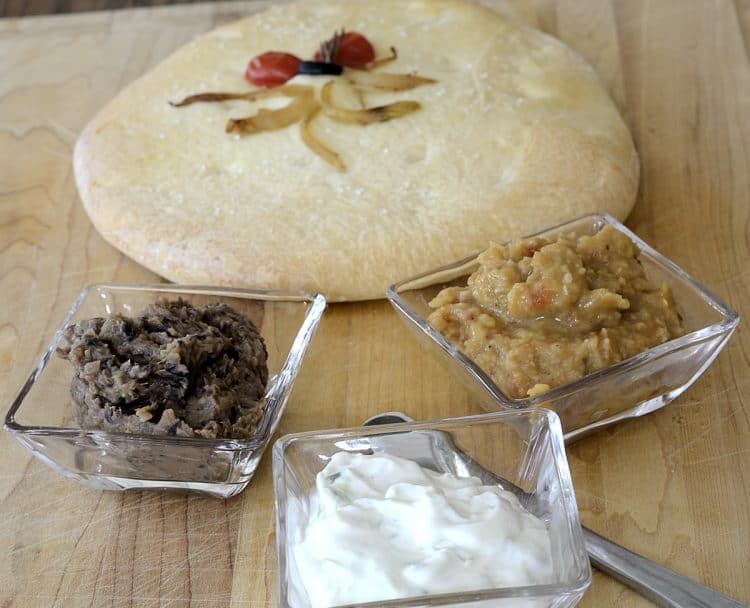 A round of focaccia bread with 3 spreads, black bean butter spread, tzatziki and curried grilled tomato spread