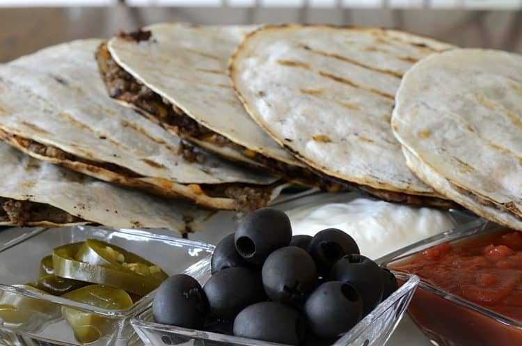 Grilled black bean quesadillas on a platter with black olives, salsa and jalapeno peppers for garnish