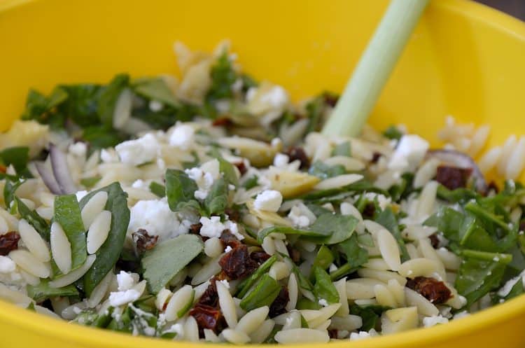 Spinach, orzo, artichoke hearts, goat cheese and sun dried tomatoes tossed in a bowl.