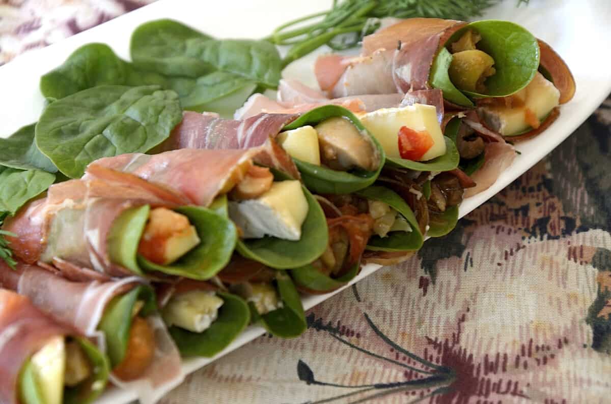 Cheese matchsticks with spinach leaves wrapped into a spiral with a prosciutto slice, on a platter